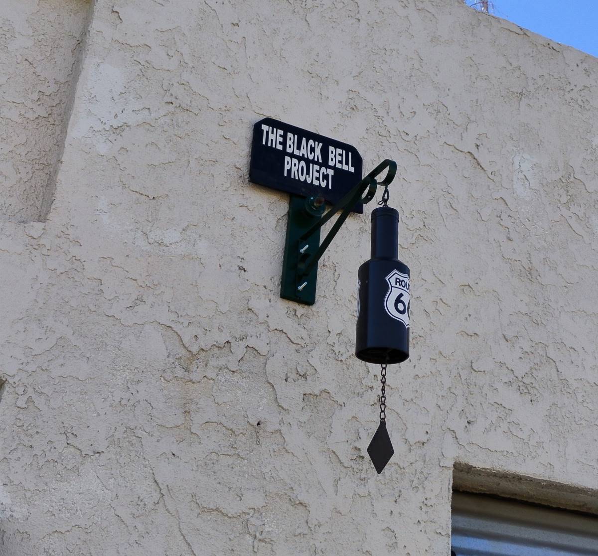 A black punching bag hanging outside a building under a sign.