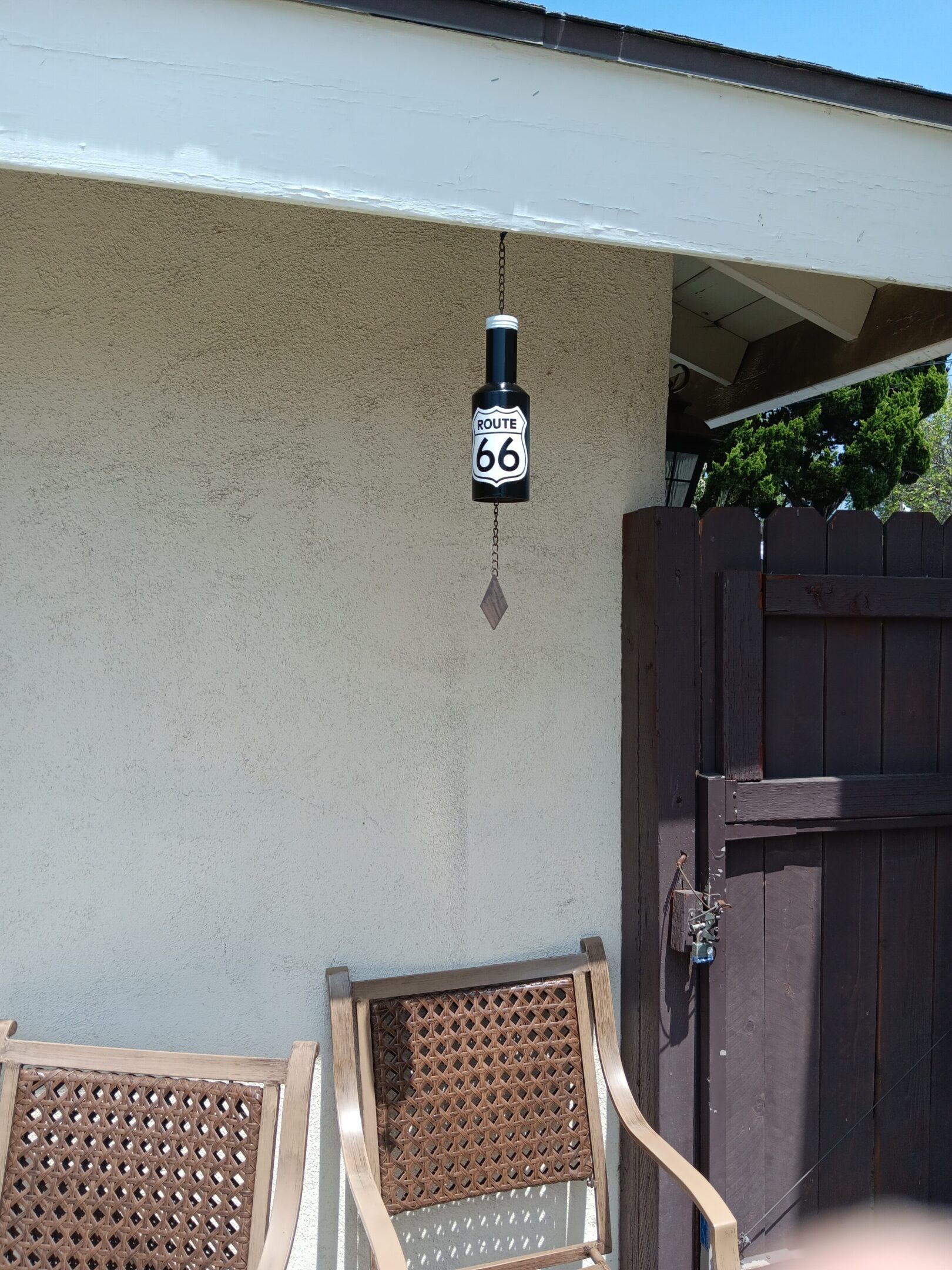 Outdoor thermometer hanging under a roof near a gate and wooden chairs.