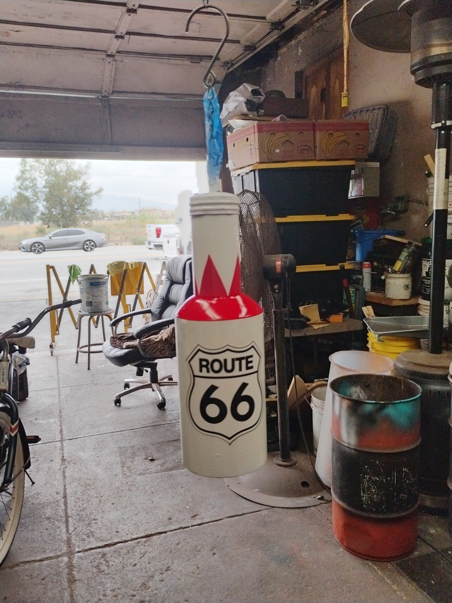 A garage workspace with a Route 66 themed trash can and various tools.