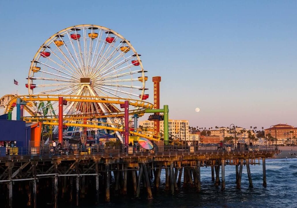Ferris wheel and amusement rides on a pier at sunset.