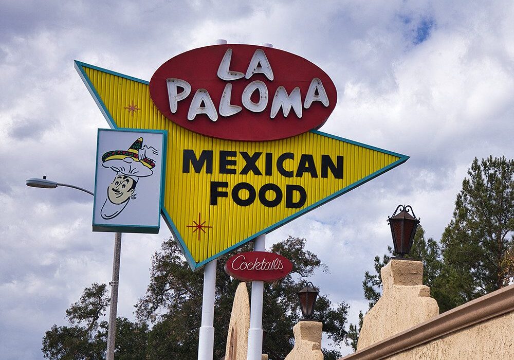Retro sign for La Paloma Mexican Food with a cloudy sky backdrop.