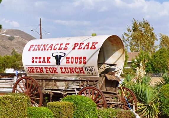 Entrance sign for Pinnacle Peak Steakhouse displayed on a covered wagon.