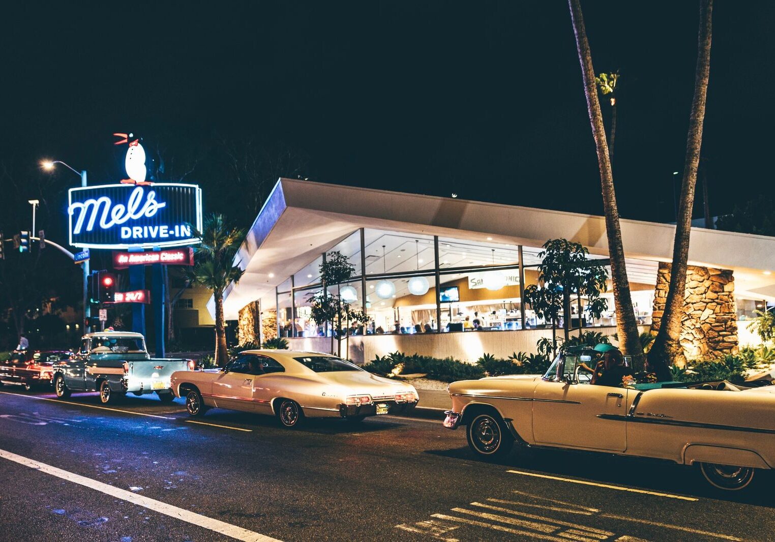 Retro diner with vintage cars parked outside at night.